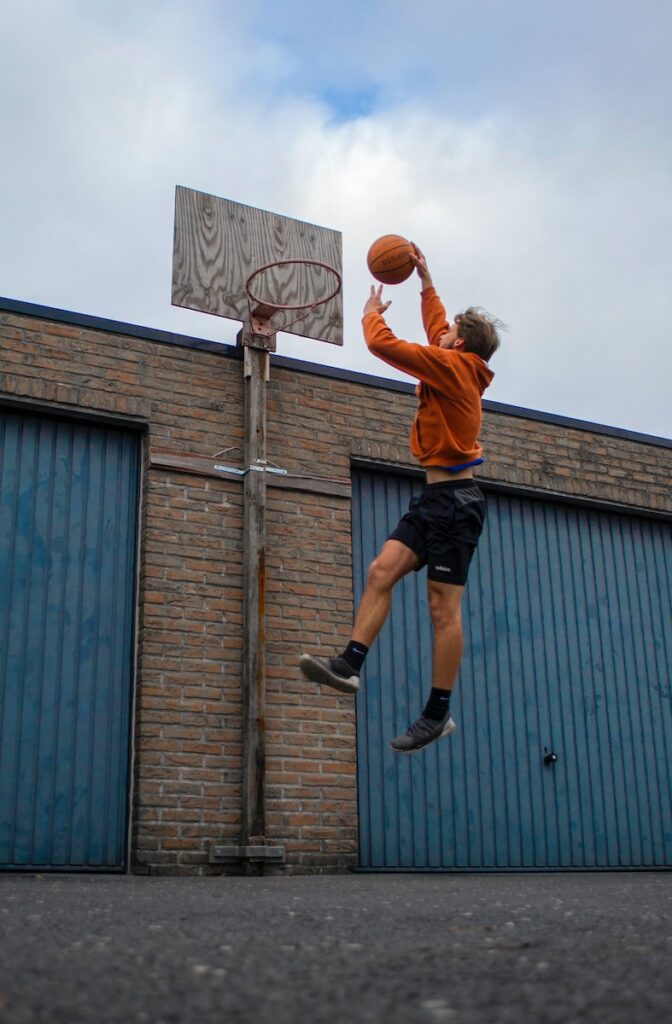 man in orange shirt and black shorts playing basketball